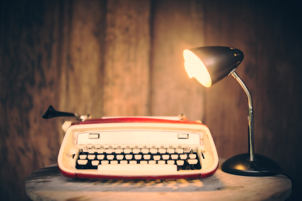 Vintage typewriter with lamp on wooden table at wooden wall background