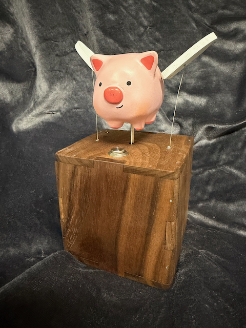 Image of a flying pig toy mounted on a wood box in front of a gray background